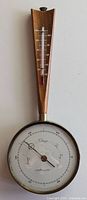 Front view showing entire barometer and thermometer mounted on wooden frame with brass accents and clear glass face.