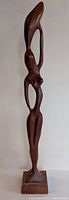 Front view of the elongated abstract carved wooden figurine on a base