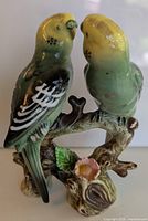 Front view of mid century ceramic parakeet figurine showing detailed painting on two birds and branch with flower