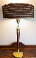 Full view of the lamp showing brown fabric shade with textured stripes and brass/wood base on wooden surface.