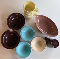 Top-down photo showing all items: dark brown bowls, aqua bowls, cream bowl, yellow mugs stacked, mauve serving bowl, and brown creamer.
