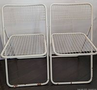 Front view of two white metal chairs with wire grid seats and backs, showing rust and wear on the frames.