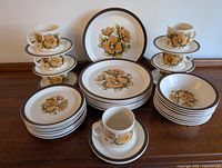 Photo showing the stacked cups, saucers, dinner plates, salad plates, and bowls that comprise the set with floral Nutwood pattern and brown rims.