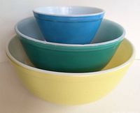 Side view of three nested Pyrex mixing bowls in yellow, cyan/green, and blue colors showing primary colors and rim details.