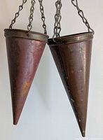 Two copper cone-shaped plant hangers suspended side by side, showing their size difference and the attached hanging chains.