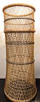 Full view of the tall rattan planter stand showing its cylindrical shape and woven construction with black accents.