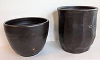 Two black glazed pottery pieces, one rounded bowl and one taller faceted cup, both signed by V. Forsyth with minor glazing imperfections.