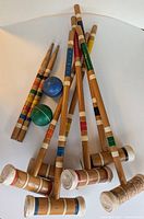 Photo showing six wooden croquet mallets with colored bands and two croquet balls on a white surface.