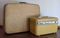Photo showing both vintage Samsonite luggage pieces, a large suitcase and a smaller cosmetics case, placed side by side on a wooden surface against a white background.