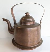 Side profile showing curved spout, hinged copper handle, broad flat base, and patina/wear.