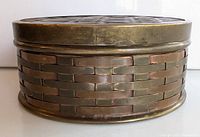 Side view of oval woven copper and brass trinket box showing the woven metal weave and brass rim.