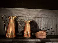 Two hammered copper pans stacked, showing their hammered texture and black handles.
