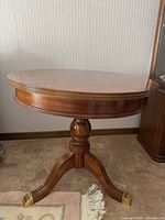 Full front view of the round mahogany rotating table showing its pedestal base with three legs capped in brass.