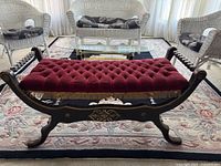 Front view of bench showing full length, red tufted velvet cushion, gold fringe trim and X-frame design.