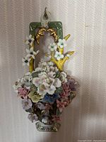 Front view of ceramic wall sconce showing detailed floral design with gold accents and green backplate.