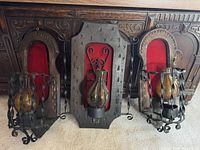 Three vintage wall sconces displayed together on the floor showing carved wood backs, red velvet fabric, and wrought iron cages with amber glass inserts.