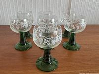 Five green stemmed French wine glasses arranged on a table.