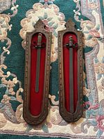 Full view of two wooden plaques with iron sword and dagger mounted on red felt.