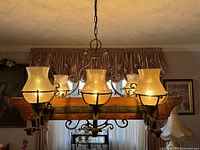 Front view of the large rustic ceiling lamp showing six amber cracked glass shades mounted on a horizontal wooden beam with metal scroll arms, lit up.