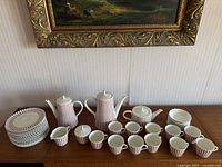 Full set of vintage Melitta coffee pots, plates, creamer, sugar bowl, cups and saucers displayed on wooden surface under framed painting, showing overall quantity and design.
