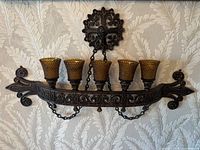 Full view of the ornate vintage entrance light fixture mounted on wall, showing five amber textured glass shades and scroll patterned metal frame with hanging chains.