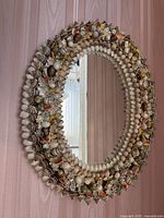 Oval seashell framed wall mirror hanging on a pink striped wallpapered wall.