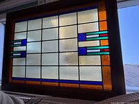Full view of the plastic stained glass window panel showing the geometric pattern and color blocks of amber-orange, blue, turquoise, and red with clear textured sections.
