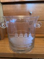 Full view of clear glass ice bucket with two round handles and etched ship design