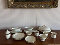 Wide shot of all porcelain serving dishes arranged on wooden table under framed painting, showing variety of items included.