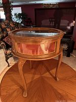 Side view of the round display table showing wood frame, glass panels, and curved legs
