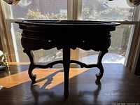 Silhouette of the entire round carved wood table front view showing three curved legs and stretcher base