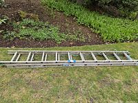 Side angle view of the Werner extension ladder laid out on grass showing full length and extension sections