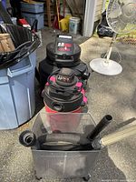 Two shop vacuums, the larger one is a Genie 25 HP model 2.5 horsepower with a hose and attachments in front.