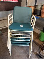 Stacked set of white metal patio chairs with teal seat and back cushions in a garage setting, showing general condition and stackability.