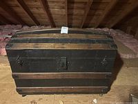 Front angled view of the antique wooden trunk showing the curved top and metal bands.
