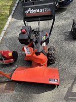 Front and side view of red Ariens ST724 housing showing chute, impeller housing and fuel tank