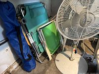 Photo showing three beach chairs folded and leaning against the wall, including teal padded reclining chair, green child chair, and blue chair with carrying bag.
