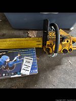 Photo of yellow McCulloch Power Mac 380 chainsaw laying on ground alongside boxed chain sharpener tool.