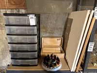 Plastic organizer shelf with six transparent drawers on left, two blank canvases, felt board on right, wooden box and round holder with paint bottles in front on table