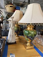 Photo showing two decorative lamps and one female statue, highlighting the lamp with painted grapevine design and a beige shade with amber bead trim.