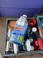 Overview of miscellaneous cleaning supplies in a crate including Windex Original bottle and assorted spray bottles.