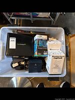 Photo of the plastic bin containing WeatherTech CupFone phone holder box, LED projection device box, Vanmass car mount, and various cables and adapters.