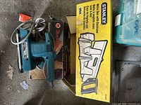 Makita hand sander resting on top of box, Stanley mitre box in yellow packaging and a hand saw beside it.