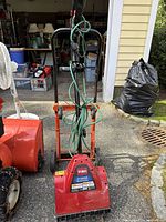 Front view of Toro electric power shovel with green power cord wrapped around handle and attached to orange and black hand truck dolly.