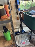 Photo of snow shovels and roof rake leaning against wall showing grips and full shovel blades.