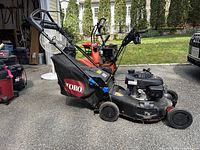 Toro push lawn mower with rear grass bag attached and foldable handlebar, parked outside