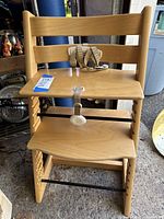 Front view of the Stokke Tripp Trapp high chair showing the adjustable seat, footrest, and attached safety harness strap.