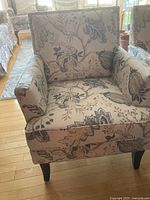 Front view of the cloth-covered arm chair showing detailed floral fabric upholstery and dark wooden legs.