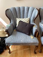Front view of blue patterned armchair with two decorative pillows placed on the seat, showing fabric's pattern and wood frame details.