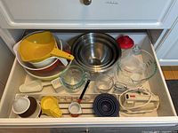 Photo showing top view of drawer with various mixing bowls, measuring cups, a hand mixer, and other related baking tools.